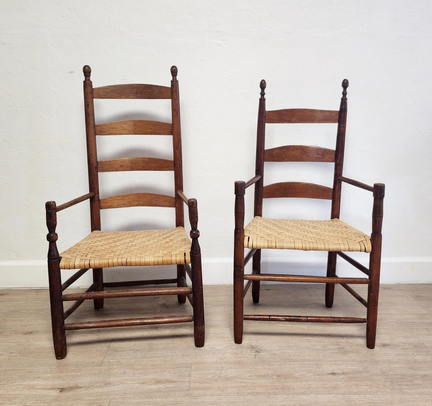 Two wooden chairs with woven seats on a wooden floor against a white wall.