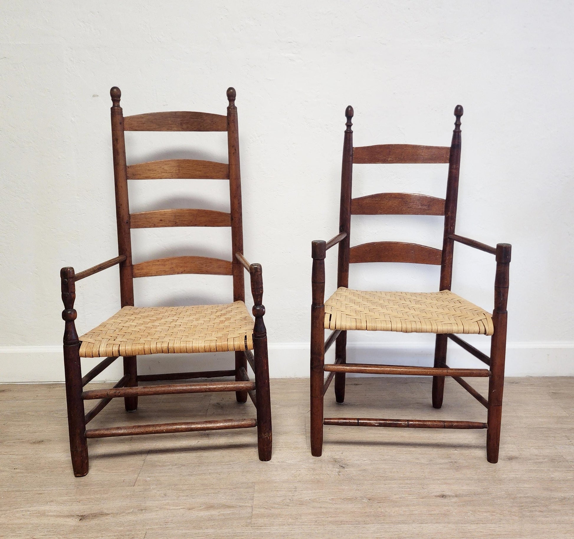 Two wooden chairs with woven seats on a wooden floor against a white wall.