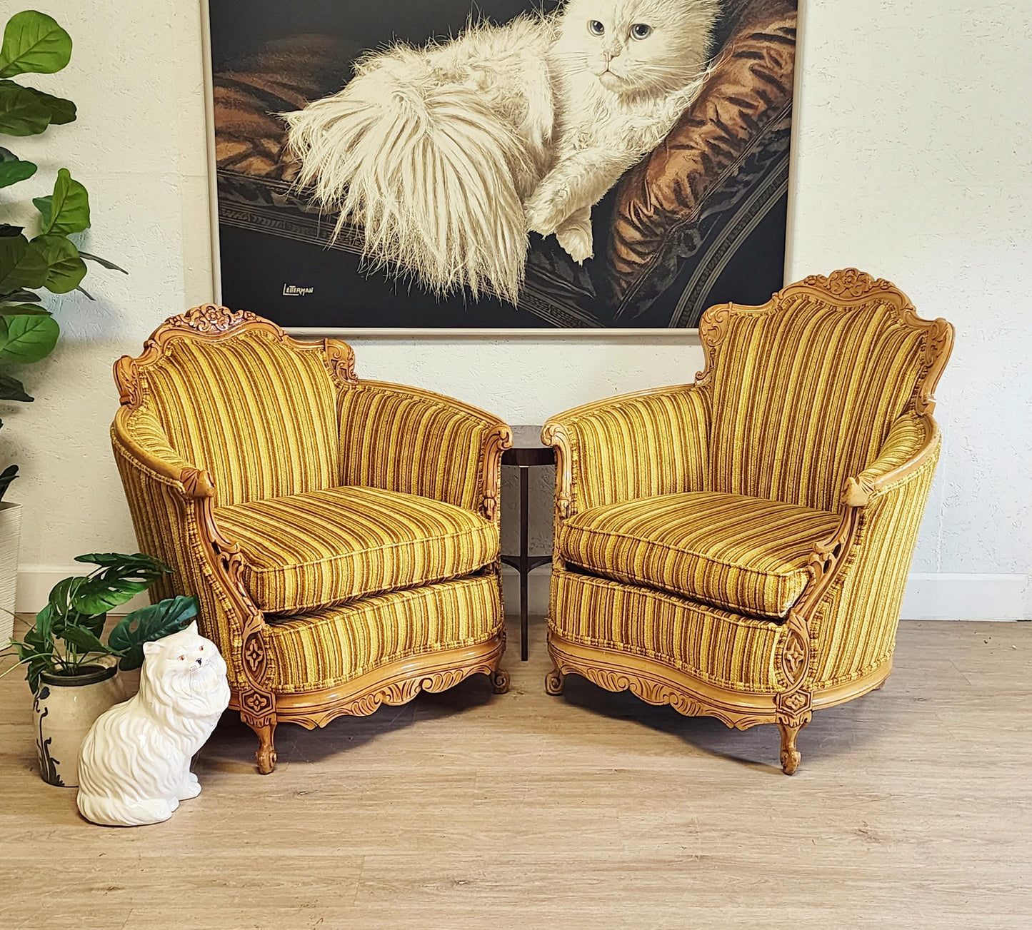 Pair of ornate yellow armchairs in a room with resting cat painting on the wall.