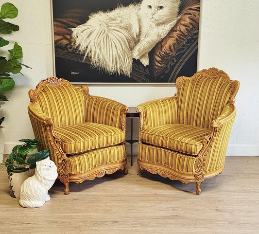 Pair of ornate yellow armchairs in a room with resting cat painting on the wall.