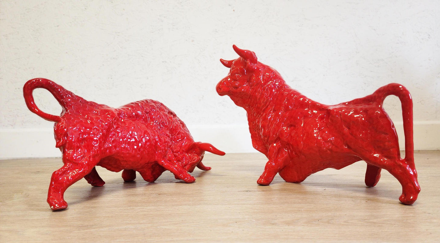Two red bull figurines on a wooden surface with a white background